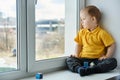 Kid sitting at home on windowsill, playing cubes and watching out the window