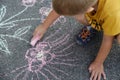 A small child in a yellow t-shirt draws chalk colored flowers on