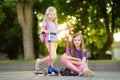 Small children learning to ride scooters in a city park on sunny summer evening. Cute little girls riding rollers.