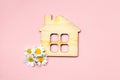 Children toy wooden house and fresh chamomile flowers on pastel pink background, sweet and ecological home concept, minimalist fla