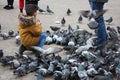 Small children on a winter day playing in a square in a European city. They enjoy chasing pigeons and feeding them Royalty Free Stock Photo