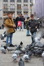 Small children on a winter day playing in a square in a European city. They enjoy chasing pigeons and feeding them Royalty Free Stock Photo