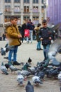 Small children on a winter day playing in a square in a European city. They enjoy chasing pigeons and feeding them Royalty Free Stock Photo