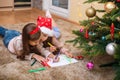 Two little sisters write the letter to Santa under the Christmas tree