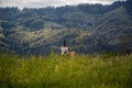 Small Christian church peaking behind meadow with hills covered in forest green trees Royalty Free Stock Photo