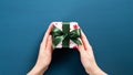 Small Christmas present with green ribbon bow in woman hands. Female hands holding gift box wrapped festive white paper over dark Royalty Free Stock Photo