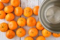 Small clementine oranges spilled onto a whitewashed wood background, empty stainless-steel bowl