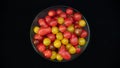 Small cocktail tomatoes, multicolored, round and oval, in a transparent glass container, on black background