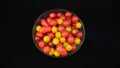 Small cocktail tomatoes, multicolored, round and oval, in a transparent glass container, on black background