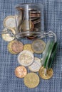 Small coins in euro cents are poured out of a glass jar on a textured blue background, selective focus, top view. A concept for bu