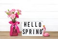 Small colored pink carnations in a vase and lightbox with text Hello Spring, flamingo figure on white wooden background Holiday Royalty Free Stock Photo