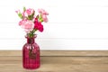 Small colored pink carnations in a vase on wooden background and white wall Hello spring, seasonal concept Mock up Place for text Royalty Free Stock Photo