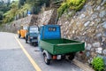 Small colorful three-wheeled trucks with a cobra park on the side of the road under a stone wall in an Italian village.