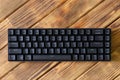 Small compact black gaming computer keyboard on a table made of wooden pine boards. Wireless keyboard with mechanical switches for Royalty Free Stock Photo