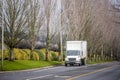 Small compact rig truck with box trailer transporting local goods on the city road with tree alley and railroad