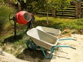 A small concrete mixer and two wheelbarrows for the manual transportation of goods are standing among greenery in the Royalty Free Stock Photo