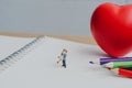 Small couple figures in love standing on notebook and red heart.