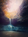 Small creek waterfall with water falling through the stone cave. Fast stream flowing down from the forest spring, through the Royalty Free Stock Photo