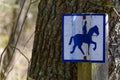 a small crooked sign in woods riding path