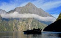 SHADOWED SHIP CRUISES BENEATH MOUNTAIN AND LOW LYING CLOUDS