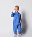Small cute baby boy in blue warm comfortable jumpsuit standing and poitning at camera with hand