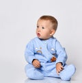 Small cute baby boy in blue warm cotton comfortable jumpsuit sitting on floor and looking aside