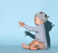 Small cute baby boy in grey comfortable jumpsuit, decorative crown on head and barefoot sitting and reaching for something