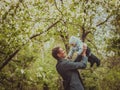 Small cute baby boy with his father walking in spring park outdoor. Man raises his little son on his hands. Blooming Royalty Free Stock Photo