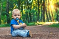 Small cute baby with nipple sits on the footpath in the dreamlike forest all alone. Little boy sitting on the ground.