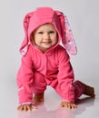 Small cute blonde positive baby girl in pink warm comfortable jumpsuit and hood wuth ears crawling on floor Royalty Free Stock Photo