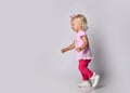 Small cute blonde smiling baby girl in pink stylish casual clothing and kitty ears running towards free copy space