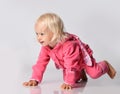Small cute cheerful blonde baby girl in pink warm comfortable jumpsuit crawling on floor Royalty Free Stock Photo