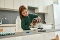 A small cute girl pouring cereal balls into a bowl with milk stainding in a large kitchen Royalty Free Stock Photo