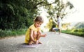 Small cute girl on a road in countryside in sunny summer nature, drawing with chalk.