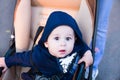 Small cute newborn baby boy sitting in a carriage in warm winter clothes with pacifier, concept of mothering autumn beanie, walk