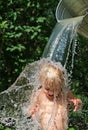 Small cute toddler boy is poured with cold water from bucket. Water games on hot day in backyard. Hardening for health. Strengthen