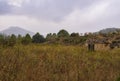 Small damaged weathered abandoned house surrounded by trees and mountains under a gray cloudy sky