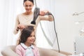 A small dark-haired girl sits in the beauty salon chair. The hairdresser dries the hair to the girl with a hairdryer. Royalty Free Stock Photo
