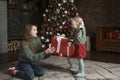 Small daughter gives big gift to her mom near Christmas tree. Portrait of mother and daughter on New Year Eve