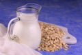 A small decanter with oat milk on a blue background.