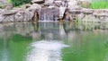 A small decorative waterfall splashes into the pond. Landscaping using stone and water in a park or garden. Natural landscape in Royalty Free Stock Photo