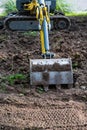 Small diesel excavator claw or bucket, resting on the ground on a dig site. Close up shot, sunny day, no people