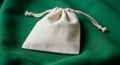 Small drawstring pouch made of cream-colored fabric resting on a textured green Royalty Free Stock Photo