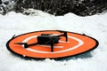 A small drone on its landing base among the cold white snow in the mountains in winter