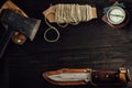 Small dusty axe, old rusty hunting bushcraft knife, military compass and a linen rope on the dark wooden table. Royalty Free Stock Photo