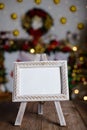 Small easel with framed blank postcard on wooden table with Christmas background.