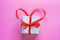 Small Elegant Gift Box Tied with Red Ribbon with Bow in Heart Shape on Pink Background. Valentine Greeting Card Wedding