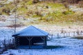 Small empty barn next to a hill between fences and grass with remnant snow Royalty Free Stock Photo