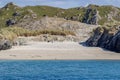 Small empty beach with calm blue water between rocky hills with green grass