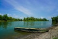 Small empty canoe by the riverbank under blue cloudy sky